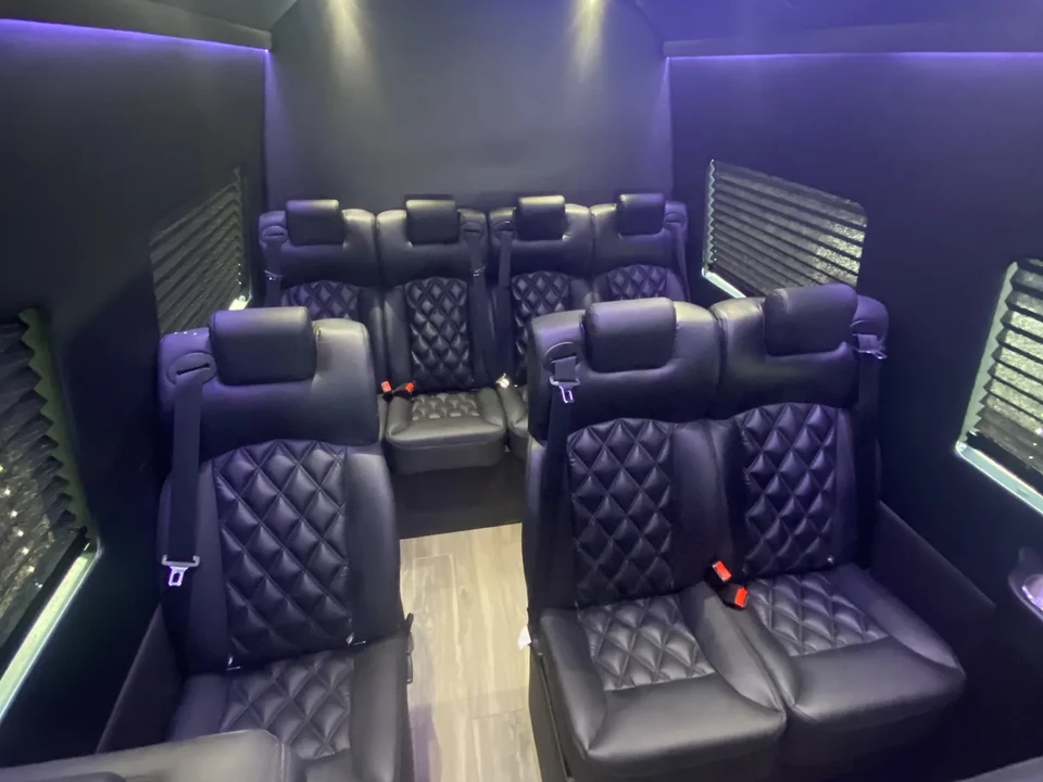 Executive Mercedes-Benz Sprinter interior with quilted black leather seating, a clear center aisle and violet ceiling lighting